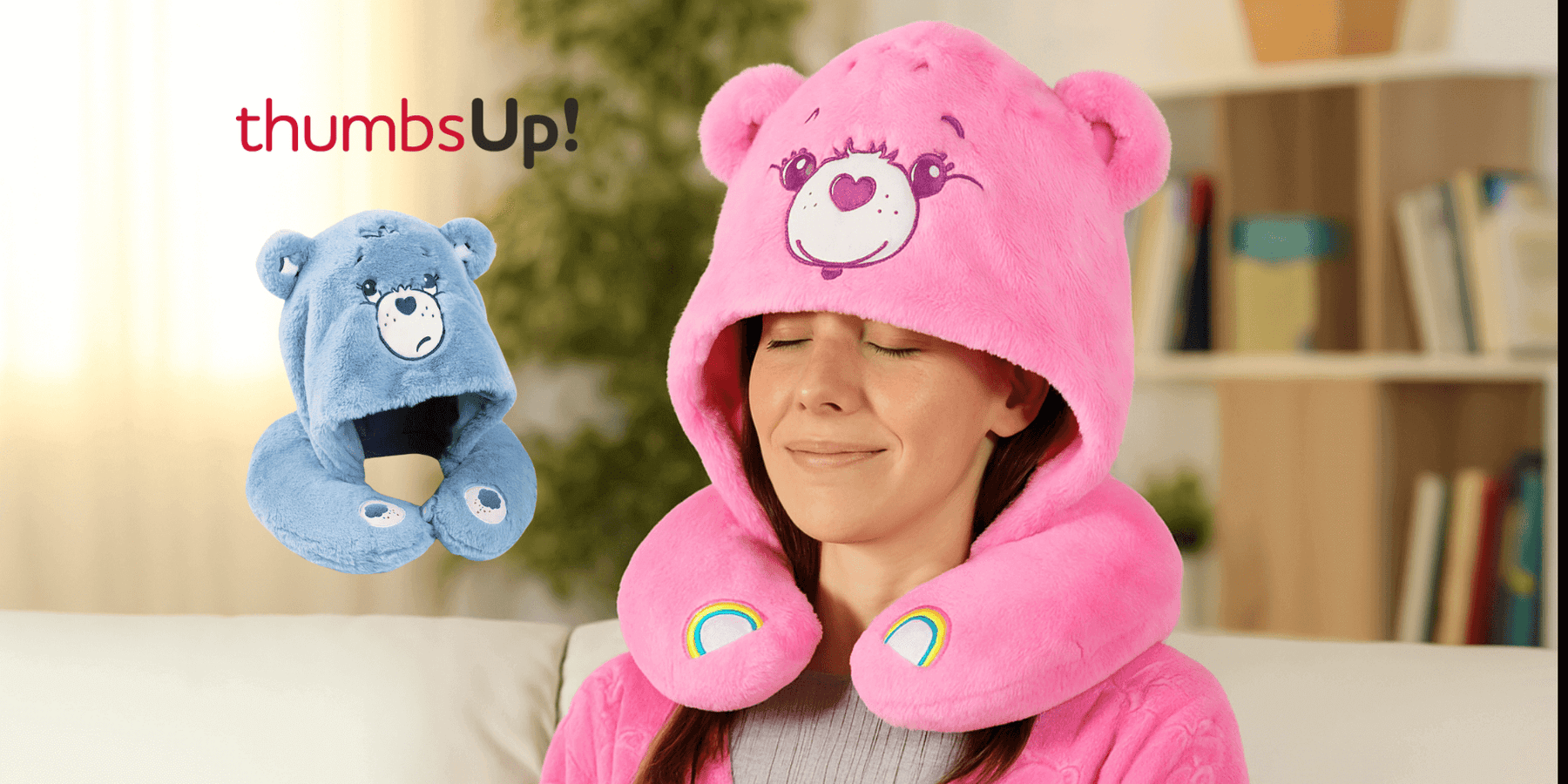 Woman wearing a pink Care Bears Snuggle Hood, enjoying comfort with a blue bear-shaped pillow beside her.