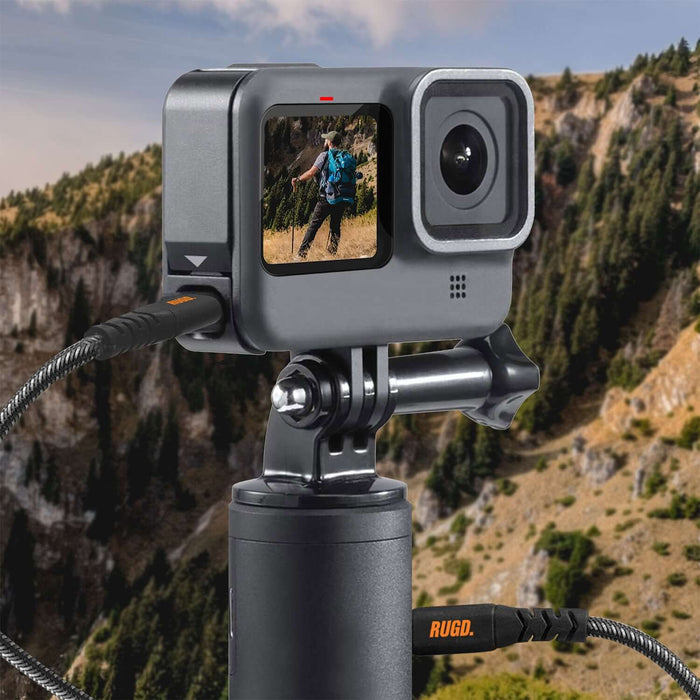 USB-C charging cable connected to a camera on a tripod, set against a mountain landscape.