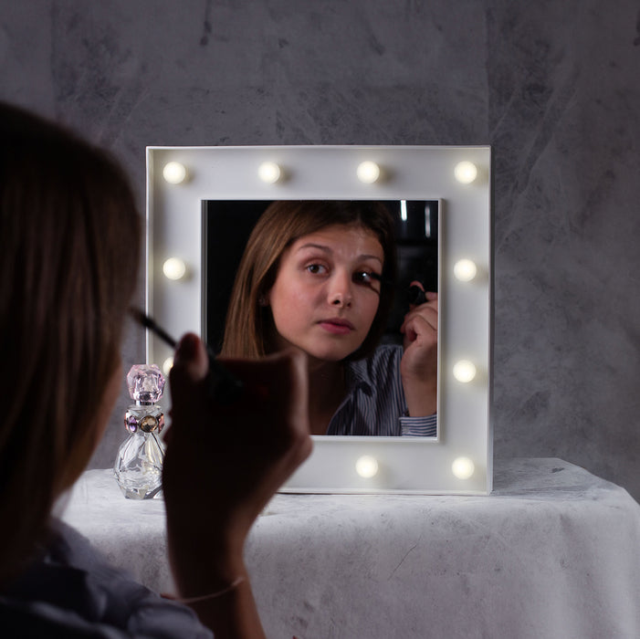 Young woman applying makeup in front of a Hollywood Mirror with LED lights, showcasing a glamorous beauty routine.
