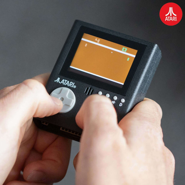 Person holding an Atari handheld console featuring a 2" LCD screen displaying Pong gameplay.