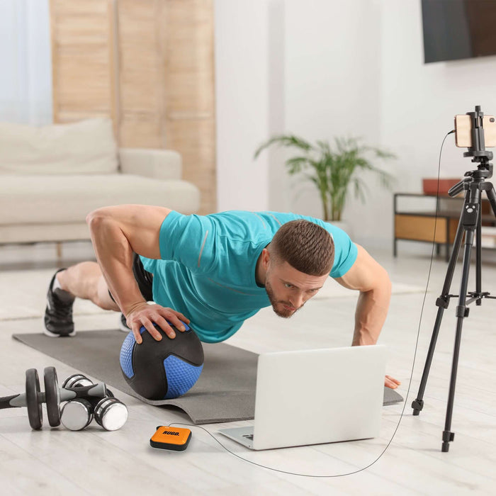 Man using a Power Bank & Camping Light while exercising indoors, watching workout video on laptop and doing push-ups with a medicine ball