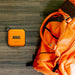 RUGD. Power Brick I Power Bank & Camping Light next to an orange backpack on a wooden surface