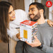 Couple holding a boxed Official Atari Beer Glass with a visible Atari logo in a cozy indoor setting.