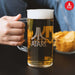 Hand holding an Official Atari Beer Glass filled with beer next to a bowl of chips.