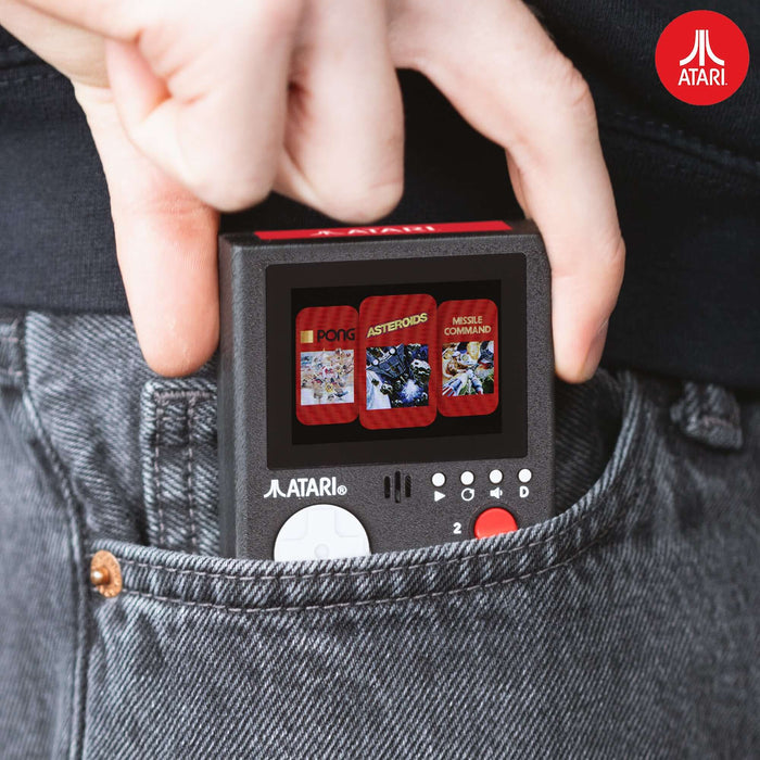 Portable Atari handheld console with Pong, Asteroids, and Missile Command games shown being placed in a pocket, featuring vibrant color LCD screen.