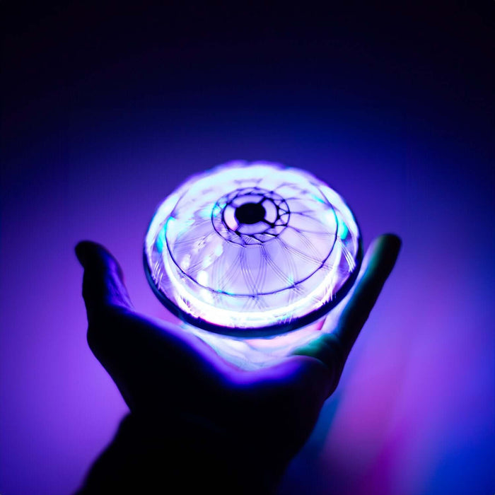 Hand holding a glowing UFO Drone with colorful LED lights against a dark background.