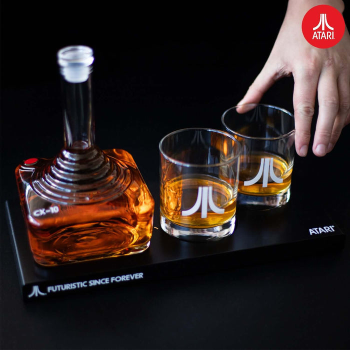 Atari joystick decanter set with two logo glasses on a tray marked "Futuristic Since Forever" and a hand reaching for a glass.