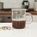 Chemistry mug with coffee inside, featuring the chemical formula C₈H₁₀N₄O₂, resembling a laboratory beaker on a kitchen countertop.