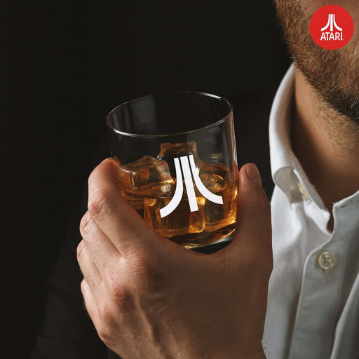 Person holding Atari branded whisky glass from decanter set with ice.